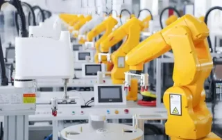 Row of yellow industrial robots in a manufacturing line, performing automated assembly on a bright factory floor.
