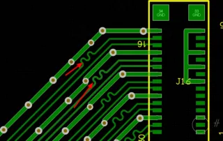 Close-up of a PCB: diagonal green signal traces with round vias, red arrows indicating bend areas, and a yellow outline around a connector area labeled J16 (GND pads nearby).