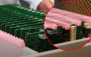 Stack of green circuit boards cushioned by pink foam padding, with a close-up of edge connectors circled in red
