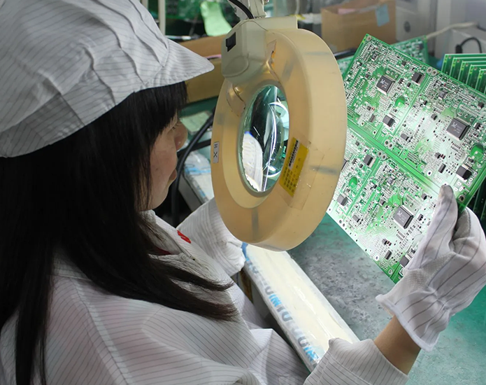 Operator inspecting a populated PCB under a magnifying lamp