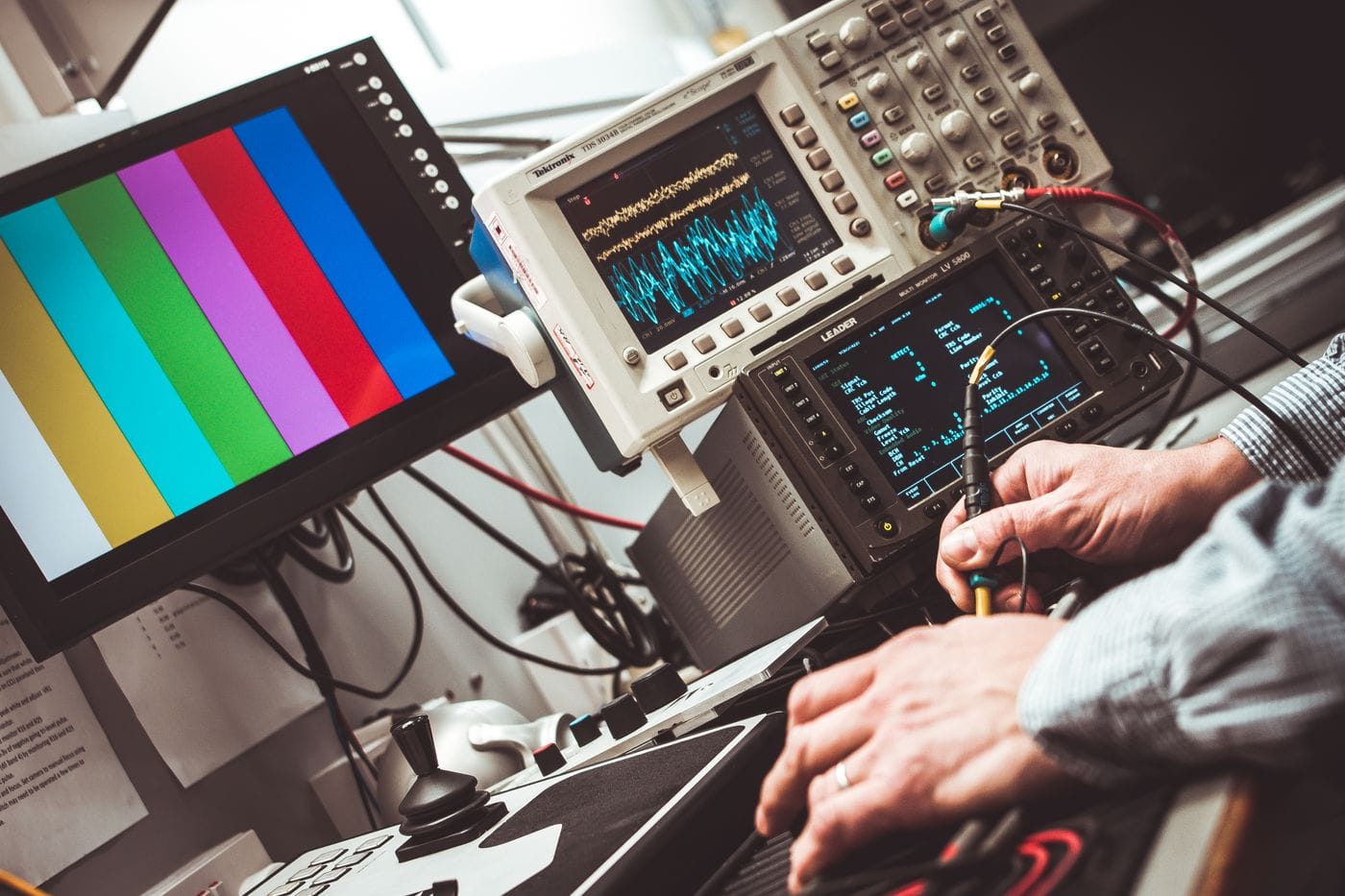 Hands operating electronic measurement equipment with waveforms displayed on laboratory instruments