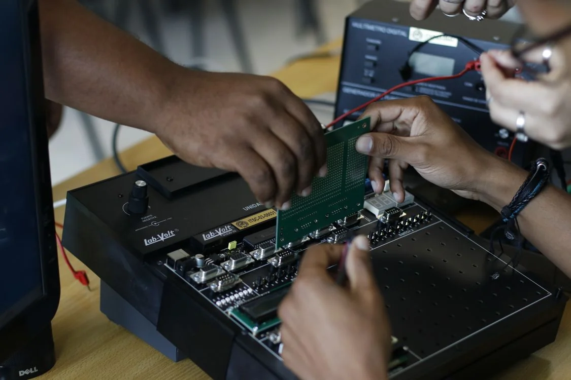 Hands working with a circuit board and an open electronic assembly on a workbench