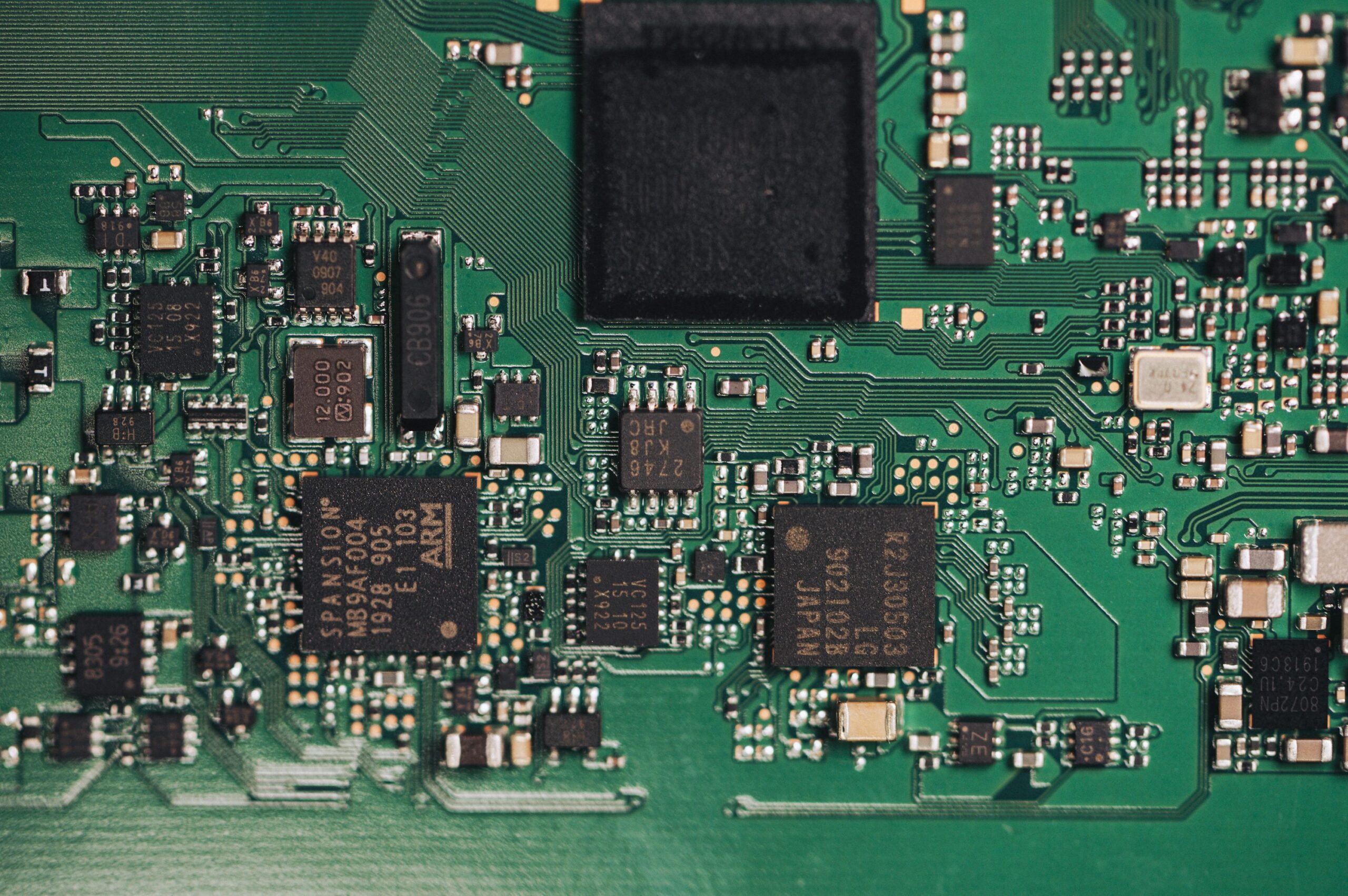 Populated green circuit board with integrated circuits, surface-mount components and visible routed traces